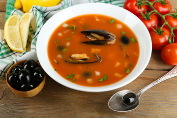 Tasty soup with mussels, tomatoes and black olives in bowl