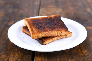Burnt toast bread on plate, on wooden table background
