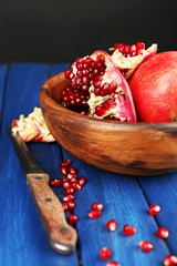 Juicy ripe pomegranates on wooden table, on dark background