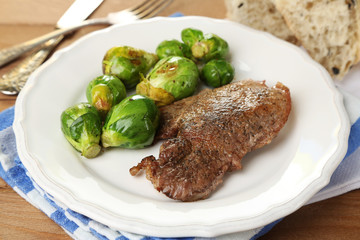 Roasted meat and vegetables on plate, on wooden table