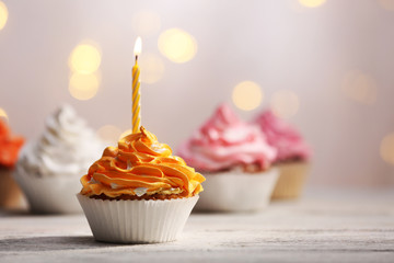 Delicious birthday cupcakes on table on light background
