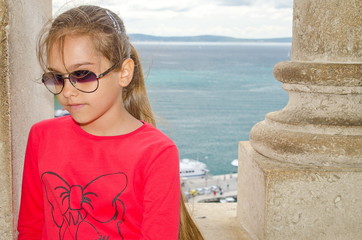 Fototapeta na wymiar girl in a red jacket and sunglasses standing between columns
