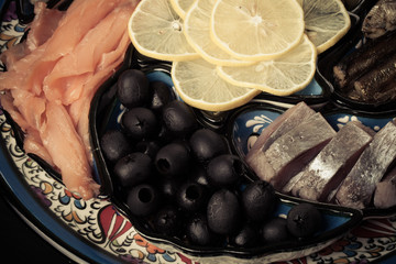 Assorty of fish, olives, lemon slices on oriental dish. Toned