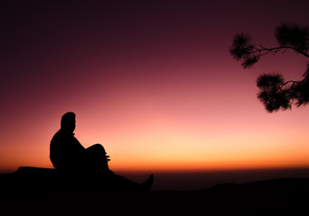 Fototapeta na wymiar silhouette of man sitting on rock