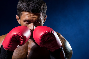 Fototapeta na wymiar Strong muscular boxer in red boxing gloves on a blue background.