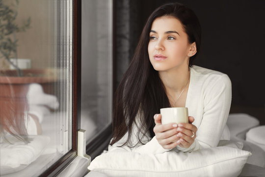 Portrait of a young woman by the window with a cup of coffee.