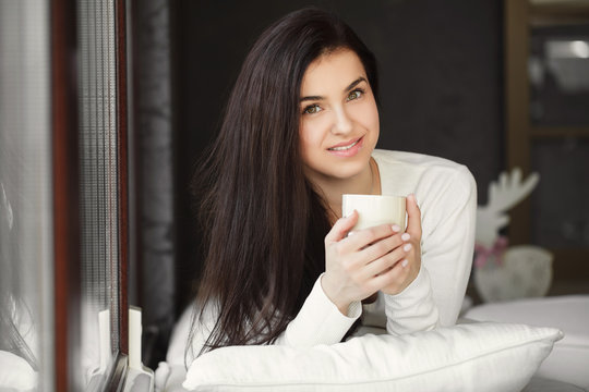 Portrait of a young woman by the window with a cup of coffee.