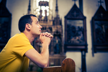 Handsome young man praying in a church - obrazy, fototapety, plakaty