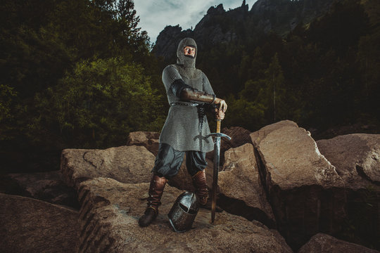 Medieval knight stands on rocks on the background of mountains