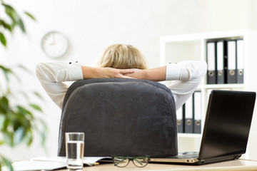 Woman relaxing in office sitting back in chair with hands behind