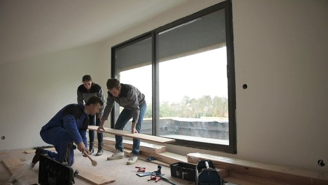 Carpenter with trainees installing wooden floor