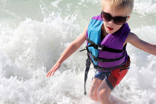 Young Child Playing in Ocean Waves in Life Jacket