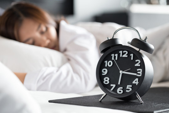 Asian woman sleeping on bed and wake up with alarm clock