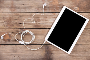 Tablet computer with earphones against wooden background