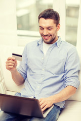 smiling man working with laptop and credit card