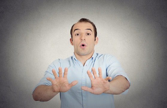 scared young man raising hand up to say no stop grey background 