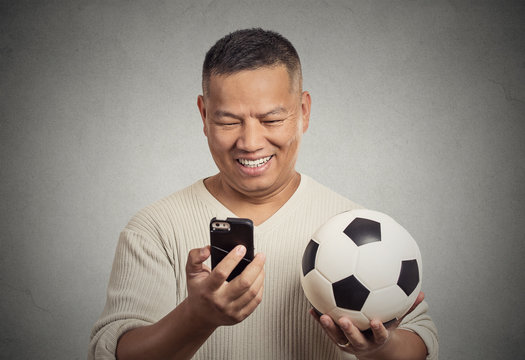 smiling man looking on smartphone watching game holding football