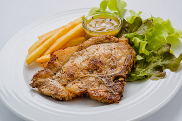 Pork steak with french fries and salad on a white background.