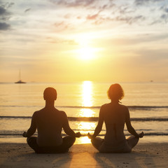 Young yoga couple is meditating on the sea beach . - obrazy, fototapety, plakaty