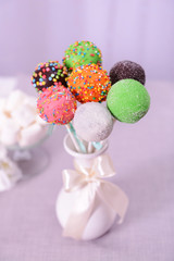 Sweet cake pops in vase on table on light background