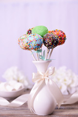 Sweet cake pops in vase on table on light background