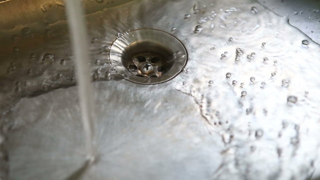water pours into the grey metal sink closeup	
