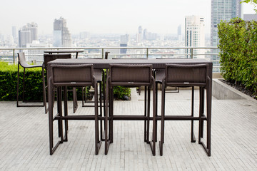 Rattan oone table with two stool chairs standing against the ter