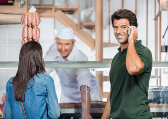 Obraz premium Happy Man On Call While Woman Buying Meat