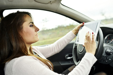 Woman driving and looking at roadmap on digital tablet