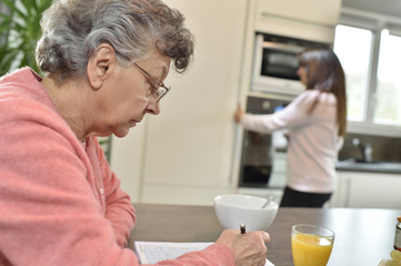 Fototapeta na wymiar Elderly woman doing crosswords while homecare helps at home