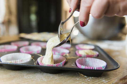A woman at a kitchen table baking fairy cakes. 