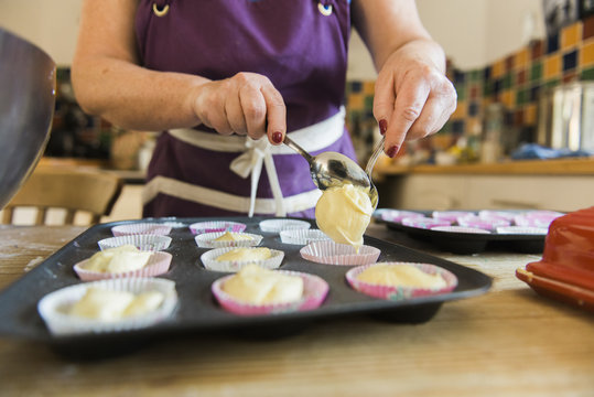 A woman at a kitchen table baking fairy cakes. 
