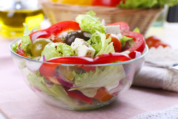 Greek salad in glass dish with fork and vegetables background