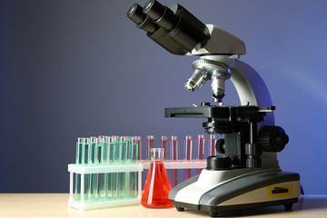 Microscope and test tubes on table, on color background