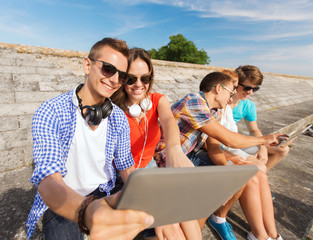 group of smiling friends with tablet pc outdoors