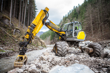 Wheeled excavator in a mountain river - obrazy, fototapety, plakaty