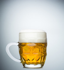 Mug with fresh beer and cap of foam on white background