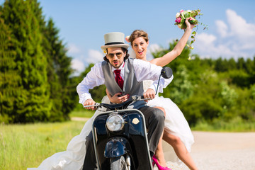 Hochzeitspaar fährt Motorroller in Hochzeitskleid und Anzug