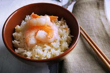 Boiled rice and shrimps in bowl, on wooden background