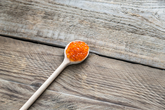 Scoop of red caviar on the wooden background
