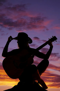 silhouette of a woman with a guitar sit hand on hat