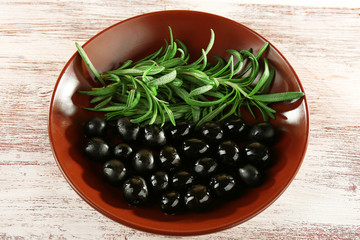 Black olive and branch in bowl on painted wooden background