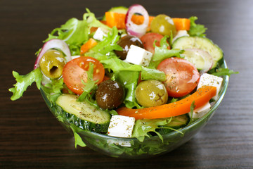 Greek salad in glass dish on wooden table background