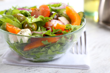 Greek salad in glass dish on napkin and color wooden background