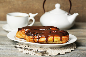 Tasty eclairs and cup of tea on wooden table