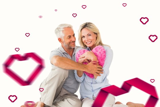 Composite image of happy couple sitting and holding heart pillow