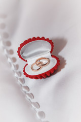 Red jewelry box with gold wedding rings on the white fabric