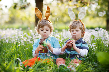 Two little boys wearing Easter bunny ears and eating chocolate