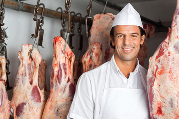 Butcher Standing Near Meat Hanging In Butchery