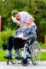 Altenpflegerin schiebt Seniorin im Rollstuhl